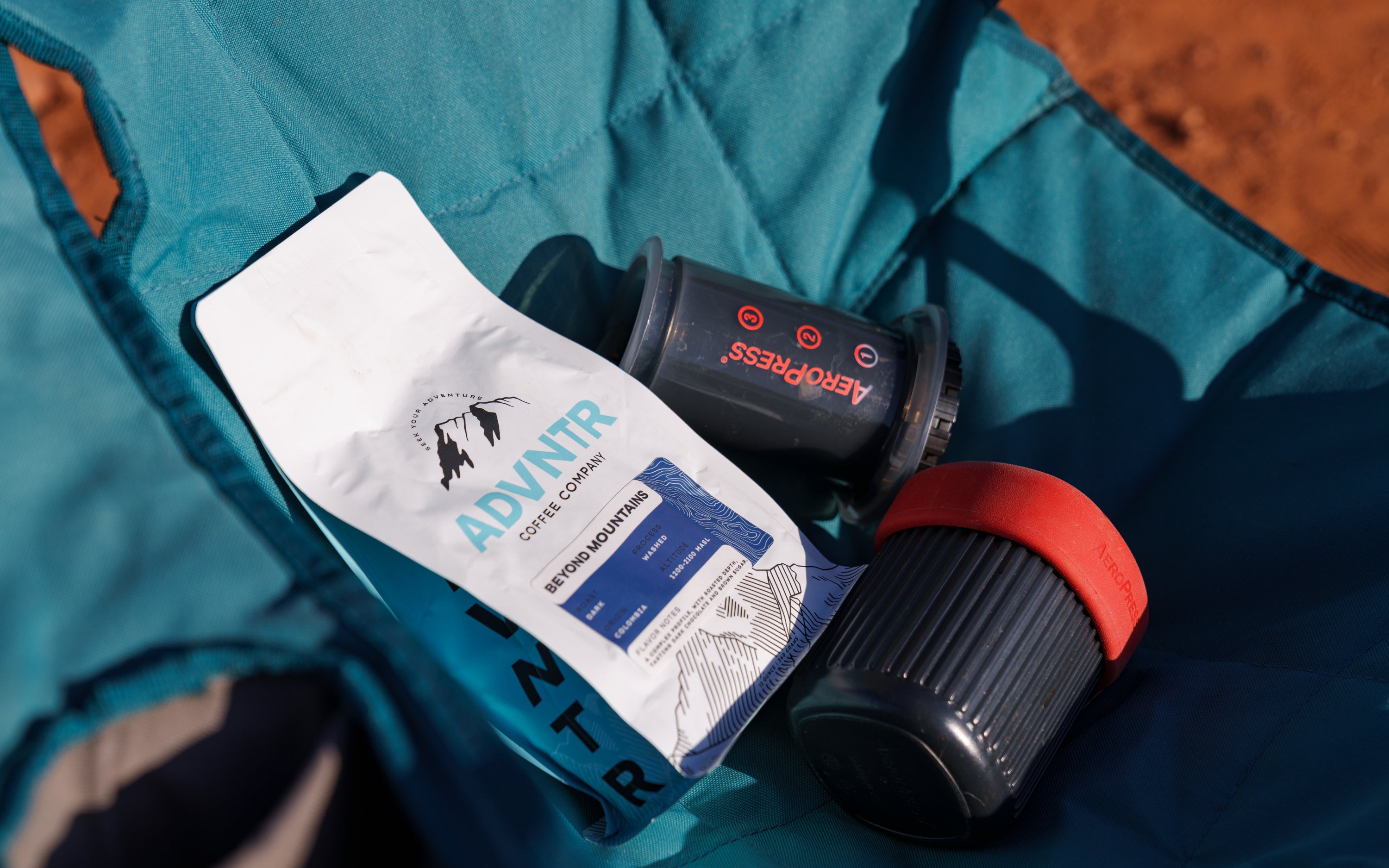 bag of ADVNTR coffee sitting on a Kelty camping chair next to Aeropress coffee maker