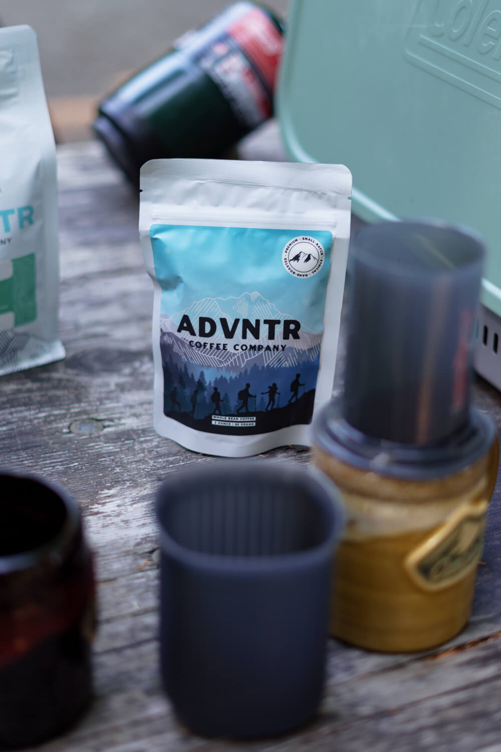 3 ounce coffee bag from adventure coffee roasters sitting on a camping table with mugs